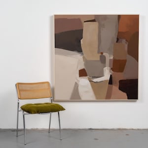 May include: An abstract painting in a gold frame, featuring a palette of browns, tans, and whites. A mid-century modern chair with a woven back and a green velvet cushion sits in front of a white wall.