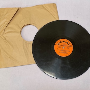 May include: A vintage black vinyl record with an orange and white label from Coral Records, next to its plain brown paper sleeve. The label reads "It's Almost Tomorrow" by Lawrence Welk and His Champagne Music.