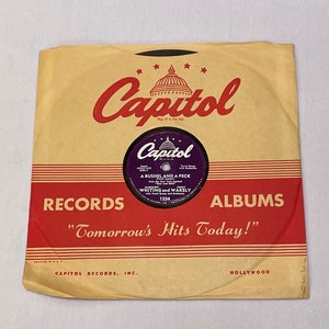 May include: Vintage Capitol Records album cover in tan and red. The Capitol Records logo is at the top, with the text "Tomorrow's Hits Today!" at the bottom. The record label is purple with the song title "A Bushel and a Peck".
