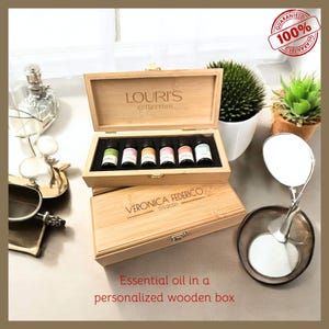 May include: A wooden box with a personalized inscription "Veronica Federico 12132023" and the text "Louri's collection" on the lid. The box contains six small glass bottles with colorful liquids inside. The box is sitting on a table with a white surface.