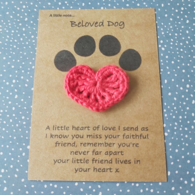May include: A brown card with the text "Beloved Dog" and a black paw print with a pink crocheted heart on top. The card reads "A little heart of love I send as I know you miss your faithful friend, remember you're never far apart your little friend lives in your heart x."