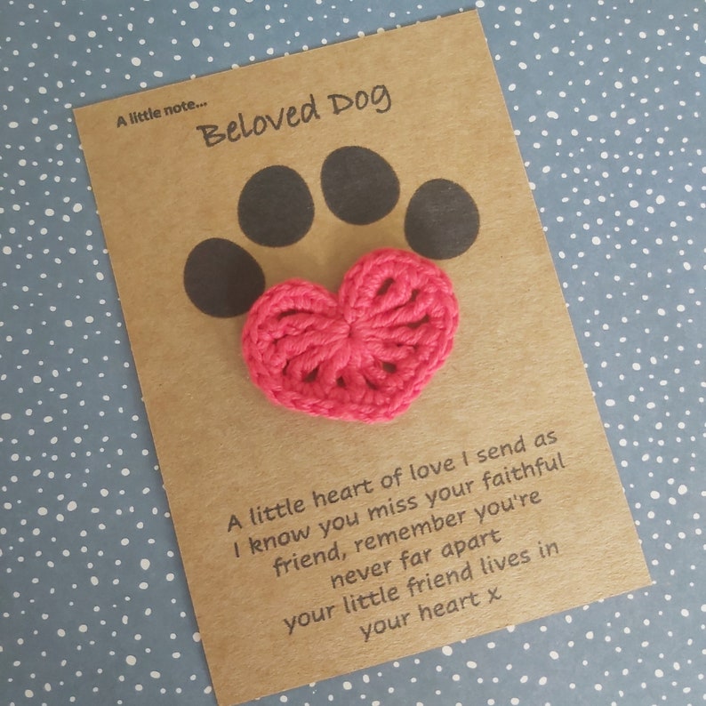 May include: A brown card with the text "A little note... Beloved Dog" and a pink crocheted heart with a black paw print behind it. The text on the card reads: "A little heart of love I send as I know you miss your faithful friend, remember you're never far apart your little friend lives in your heart x"