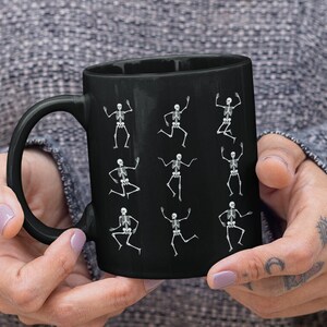 May include: Black coffee mug with a white skeleton design. The skeletons are in various dancing poses.