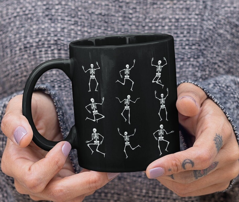 May include: Black coffee mug with a white skeleton design. The skeletons are in various dancing poses.