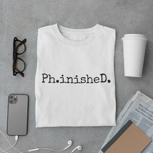 May include: White t-shirt with the text "Ph.inisheD." printed in black.