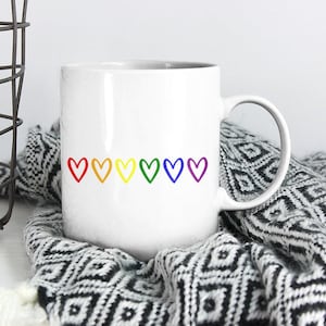 May include: White ceramic mug with a row of rainbow-colored hearts printed on the front.