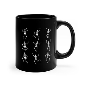 May include: Black ceramic coffee mug with a white design of multiple skeletons dancing.