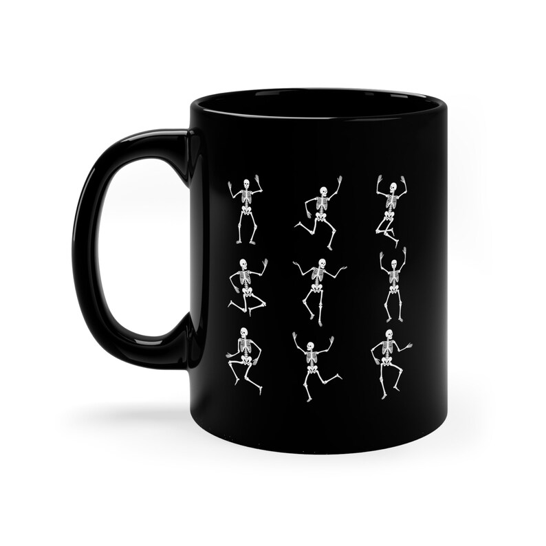 May include: Black ceramic coffee mug with a white design of skeletons dancing. The mug has a white handle.