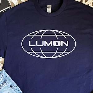 May include: A navy blue t-shirt with a white graphic of a globe with the word "LUMON" inside.