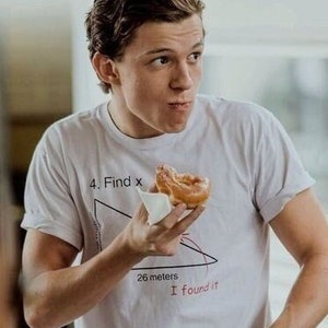 May include: A person wearing a white t-shirt with a math problem printed on it. The problem is a right triangle with the text "4. Find x" and "26 meters" written on it. The person is holding a donut in their right hand.