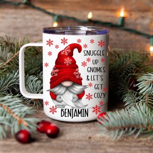 May include: White ceramic mug with a red and white gnome design. The mug has a handle and says "Snuggle Up Gnomes & Let's Get Cozy" with the name "Benjamin" at the bottom.