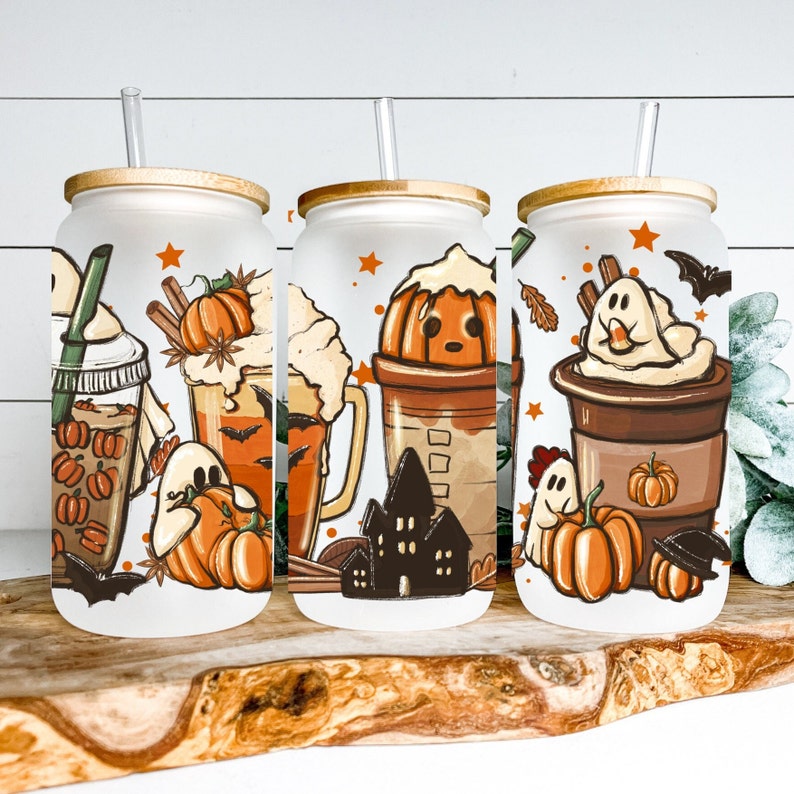May include: Three white tumblers with lids and straws, featuring Halloween-themed designs. Each tumbler has a different design with pumpkins, ghosts, and coffee drinks.