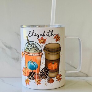 May include: White travel mug with a personalised name "Elizabeth" and a fall-themed design featuring two coffee cups, pumpkins, and autumn leaves.