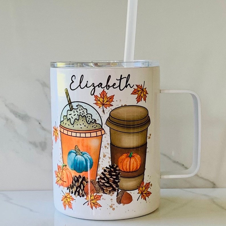 May include: White travel mug with a personalised name "Elizabeth" and a fall-themed design featuring two coffee cups, pumpkins, and autumn leaves.