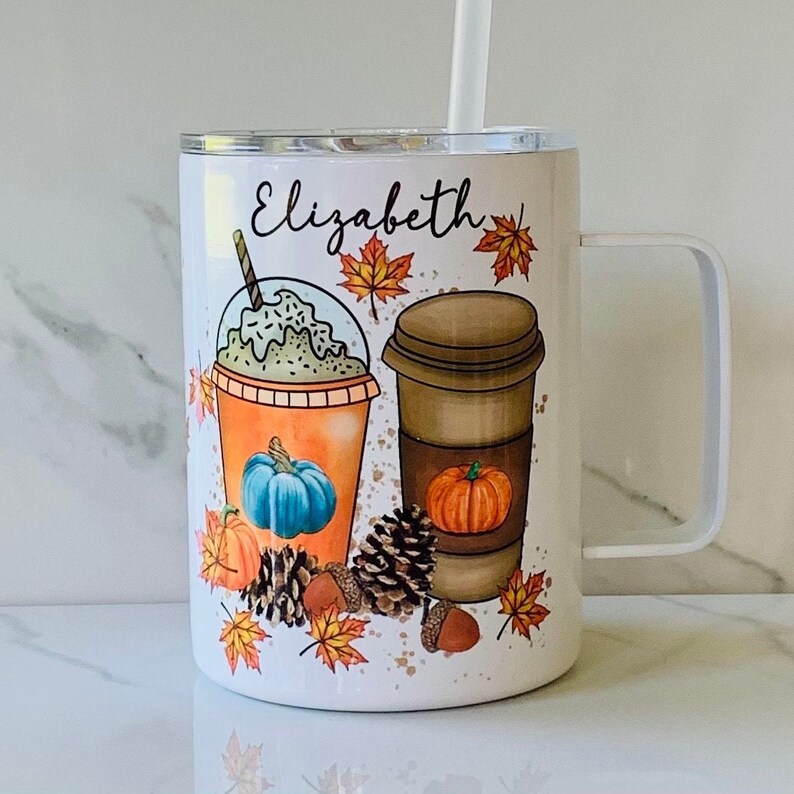 May include: White stainless steel tumbler with a handle. The tumbler features a fall-themed design with a pumpkin spice latte, a pumpkin milkshake, and autumn leaves. The tumbler is personalised with the name "Elizabeth".