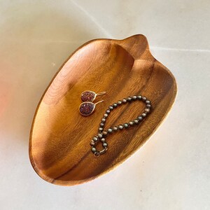 Op de afbeelding: Een houten kom in de vorm van een hart met een parelketting en een paar oorbellen erin.