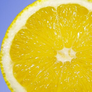 Könnte beinhalten: Nahaufnahme einer saftigen, halbierten Orange vor hellblauem Hintergrund. Das Fruchtfleisch ist leuchtend gelb, mit weißer Schale und gelb-grüner Schale. Die Textur der Orange ist deutlich erkennbar.