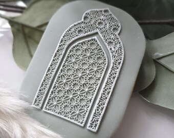 May include: A light green, oval-shaped, decorative wall hanging with a white, intricate, geometric design resembling an archway.