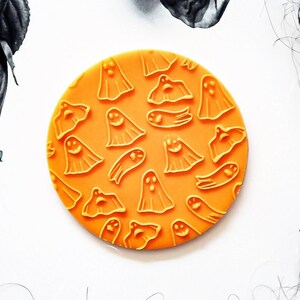 May include: Orange round silicone stamp with a repeating pattern of ghosts. The ghosts are in various poses and have different facial expressions.