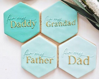 Könnte beinhalten: Vier sechseckige Kekse, verziert mit hellblauem Zuckerguss und goldenen Buchstaben. Die Kekse sagen "for my Daddy", "for my Grandad", "for my Father" und "for my Dad".