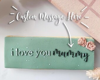 May include: A light green rectangular cookie with the text "i love you mummy" in black lettering. The cookie is decorated with pink sugar flowers.