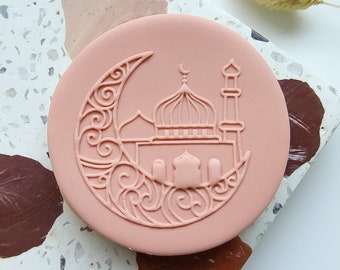 May include: A pink cookie cutter with a detailed design of a mosque and crescent moon. The cookie cutter is on a white and brown speckled surface.