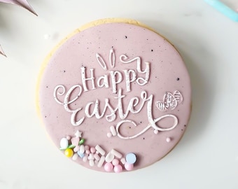 May include: A pink iced sugar cookie decorated with white icing and the words "Happy Easter". The cookie is surrounded by colorful sprinkles.