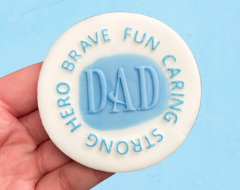 May include: White round cake topper with blue lettering that says "HERO BRAVE FUN CARING STRONG" in a circle around the word "DAD" in a blue circle.