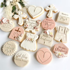 Puede incluir: Surtido de galletas de az&uacute;car decoradas para un bautizo. Las galletas presentan varios dise&ntilde;os, incluyendo una cruz, un coraz&oacute;n, un vestido, un mono de beb&eacute; y un cartel con el texto "D&iacute;a del Bautismo de [Nombre]".