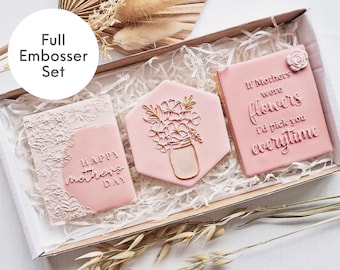 May include: A set of three pink cookies with embossed designs. The cookies are in a white box with shredded paper. The cookies have the following text: "Happy Mother's Day", "If Mothers were flowers I'd pick you everytime", and a floral design with a jar.