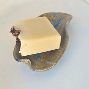 May include: A ceramic soap dish with a blue and brown glaze. The dish is shaped like a leaf and has a raised edge to hold soap. A bar of soap is sitting in the dish.