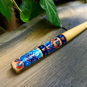 May include: A hand-painted wooden pipe with a floral design in blue, red, and orange. The pipe has a light-colored body and a dark blue band with a floral pattern. The pipe is approximately 6 inches long.