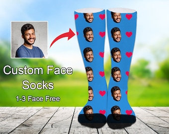 May include: A pair of blue knee-high socks with a repeating pattern of red hearts and a man's face. The socks are shown on a wooden surface with a green grassy background. "Custom Face Socks 1-3 Face Free" is written in white text on a black background.