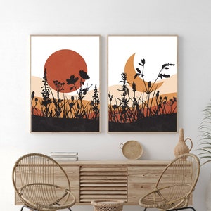 May include: Two framed art prints featuring a minimalist landscape design. One print shows a large orange sun, the other a crescent moon, both set against a field of black silhouettes of plants and grasses. The prints are in wooden frames.