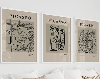 May include: Three framed Picasso art prints. Each print features a black line drawing on a beige background, with the name "Picasso" at the top. The prints are displayed above a white sofa with decorative pillows and a throw blanket.