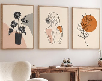 Pode incluir: Três impressões de arte emolduradas com designs minimalistas. Uma apresenta uma planta preta num vaso escuro, outra um desenho de linha de uma mulher e a terceira um ramo com um círculo laranja. As molduras são de cor castanho claro.