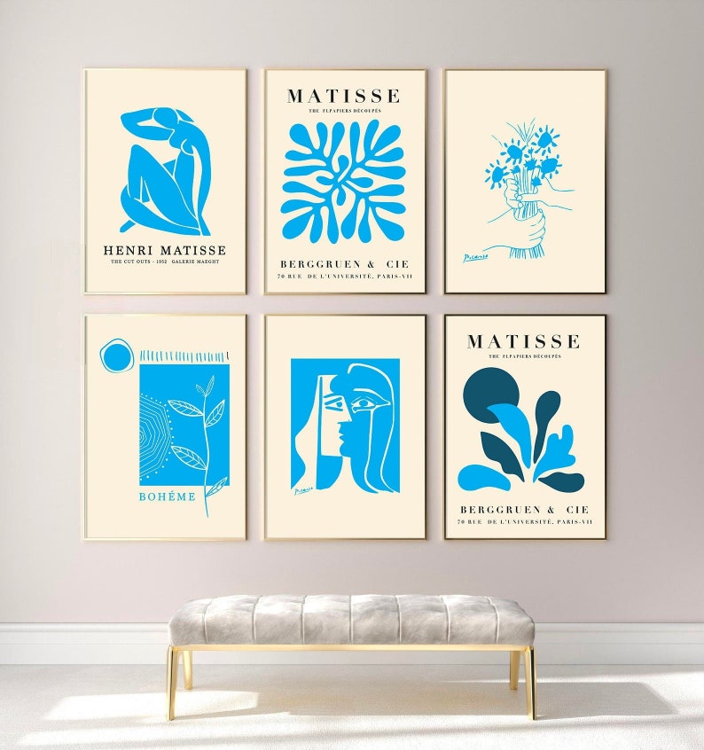 Op de afbeelding: Zes ingelijste kunstprints met blauwe en cr&egrave;mekleurige kleurenschema's. De prints tonen abstracte ontwerpen, figuren en tekst, waaronder de namen "Matisse" en "Picasso". Onder de kunstwerken staat een bank met een grijze fluwelen zitting.
