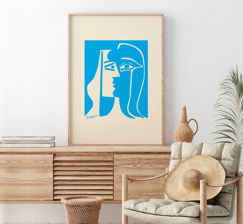 Op de afbeelding: Een ingelijste kunstdruk met een blauw en wit abstract portret. Het kunstwerk, gesigneerd door Picasso, toont het profiel van een vrouw met gedurfde, geometrische vormen. De print wordt gepresenteerd op een lichtbeige achtergrond en voegt een vleugje moderne kunst toe.