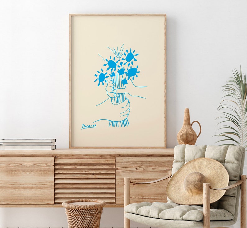 Op de afbeelding: Een ingelijste kunstdruk met een blauwe lijntekening van een boeket bloemen, vastgehouden door handen. Het kunstwerk staat op een cr&egrave;mekleurige achtergrond en is gesigneerd met "Picasso". De lijst is van licht hout.