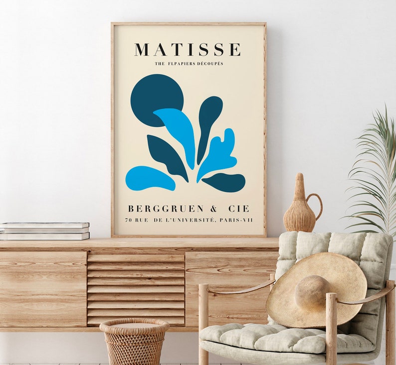Op de afbeelding: Een ingelijste kunstprint met een Matisse-ontwerp, een beige achtergrond en blauwe abstracte vormen. De print bevat de naam "MATISSE" en de tekst "THE FLPAPIERS DECOUPES" bovenaan, en "BERGGRUEN & CIE" en een adres onderaan.