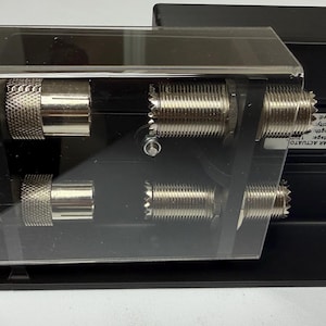 May include: A black linear actuator with silver connectors and a clear plastic cover. The device has a rectangular base with mounting holes and a label with technical specifications. The actuator is designed for mechanical applications.