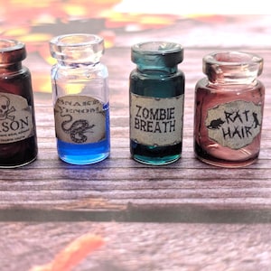 以下が含まれることがあります： 「POISON」「SNAKE VENOM」「ZOMBIE BREATH」「RAT HAIR」と書かれたラベルが付いた、4つの小さなガラス製のポーションボトル。ボトルにはカラフルな液体が入っており、木製の表面に配置されています。ラベルはヴィンテージ感があります。