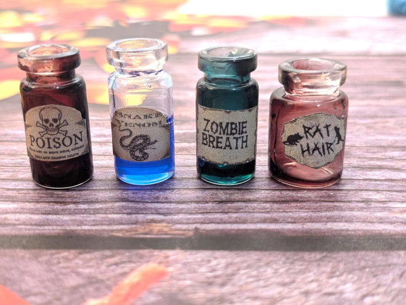 以下が含まれることがあります： 「POISON」「SNAKE VENOM」「ZOMBIE BREATH」「RAT HAIR」と書かれたラベルが付いた、4つの小さなガラス製のポーションボトル。ボトルにはカラフルな液体が入っており、木製の表面に配置されています。ラベルはヴィンテージ感があります。
