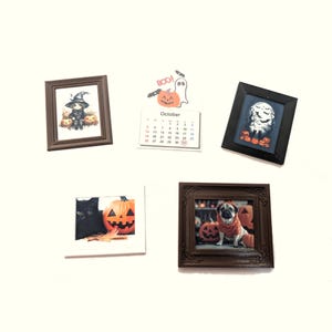 以下が含まれることがあります： ハロウィーンをテーマにしたミニチュアの額入り写真とカレンダーのコレクション。写真には魔女、幽霊、黒猫、衣装を着たパグ、カボチャが写っています。カレンダーは10月を示しています。