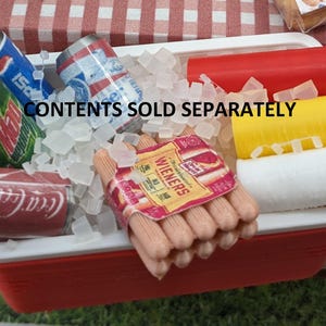 May include: A miniature red and white cooler filled with ice cubes, soda cans, and a package of wieners. The cooler also contains red ketchup and yellow mustard bottles. The text "CONTENTS SOLD SEPARATELY" is visible.