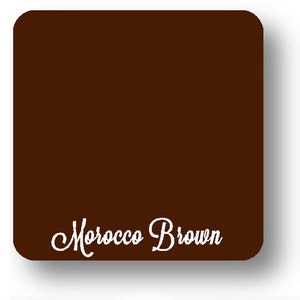 May include: A square, dark brown object with rounded corners. The words "Morocco Brown" are written in a cursive font across the bottom of the object. The background is white.