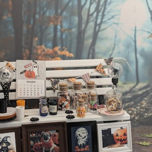 以下が含まれることがあります： 白いベンチに飾られたミニチュアハロウィーンディスプレイ。カレンダー、額入りの写真、お菓子が入ったガラス瓶、装飾ライト、バナーが特徴です。10月のカレンダーと不気味な装飾が、お祝いの雰囲気を醸し出しています。