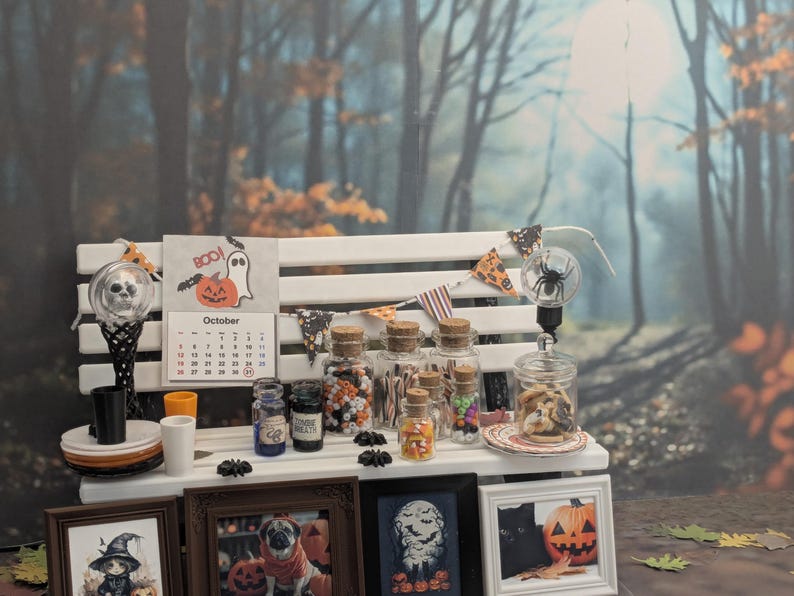 以下が含まれることがあります： 白いベンチに飾られたミニチュアハロウィーンディスプレイ。カレンダー、額入りの写真、お菓子が入ったガラス瓶、装飾ライト、バナーが特徴です。10月のカレンダーと不気味な装飾が、お祝いの雰囲気を醸し出しています。