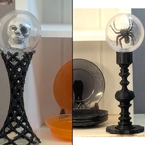以下が含まれることがあります： ハロウィーンをテーマにした2つの装飾キャンドルホルダー。1つは、黒い格子模様のベースの上に、透明なグローブの中に頭蓋骨があります。もう1つは、黒い装飾ベースの上に、透明なグローブの中に黒いクモがあります。