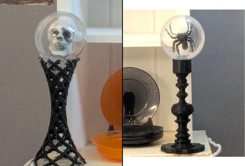 以下が含まれることがあります： ハロウィーンをテーマにした2つの装飾キャンドルホルダー。1つは、黒い格子模様のベースの上に、透明なグローブの中に頭蓋骨があります。もう1つは、黒い装飾ベースの上に、透明なグローブの中に黒いクモがあります。